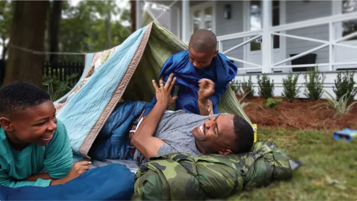 Father playing with sons while camping in yard 