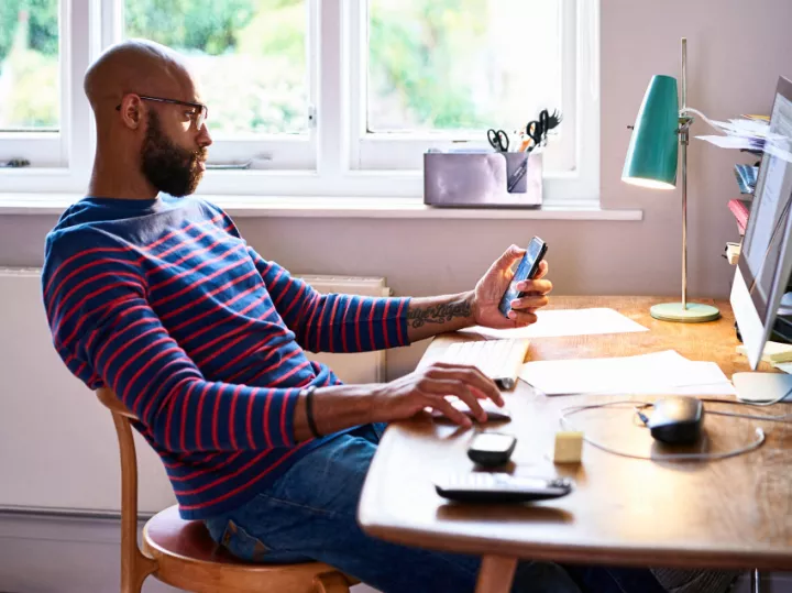 Man looking at cell phone while working at his desk.
