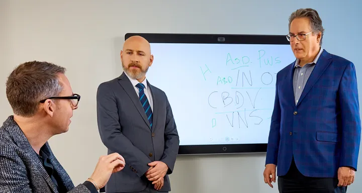 Three men in suits discussing in front of a whiteboard with handwritten notes
