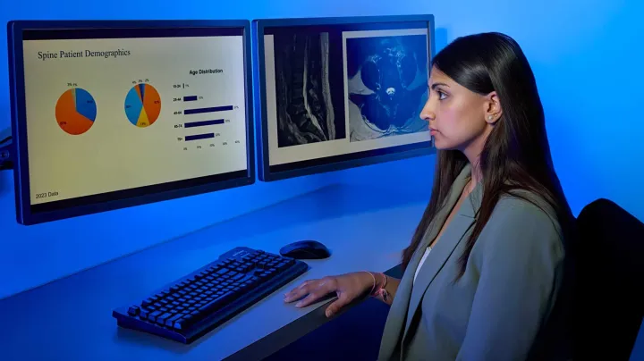 Doctor sitting at a desk, looking at 2 computer screens