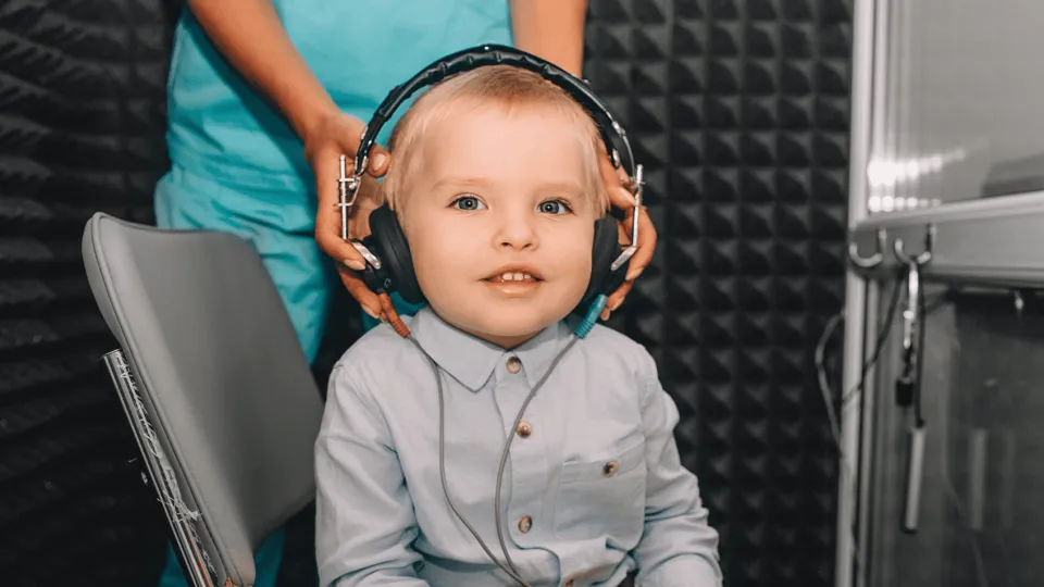 Smiling young child at auditory processing test station wearing headphones
