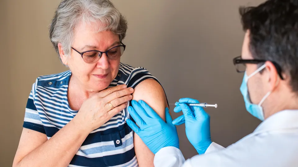 Older woman getting injected with a vaccine by doctor in upper arm