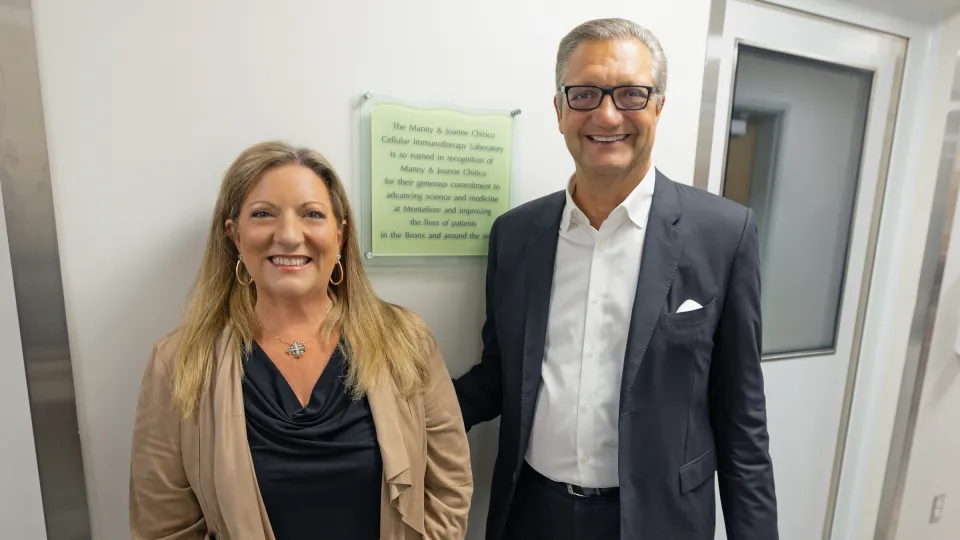 Manny and Joanne Chirico stand together in front of the dedication plaque for the Manny and Joanne Chirico Cellular Immunotherapy Laboratory at Montefiore Einstein.